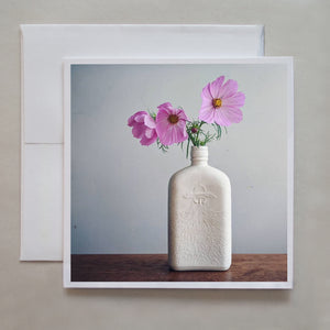Soft lighting wraps around beautiful pink flowers standing in a white bottle vase in this photograph note card by photographer Jennifer Echols.