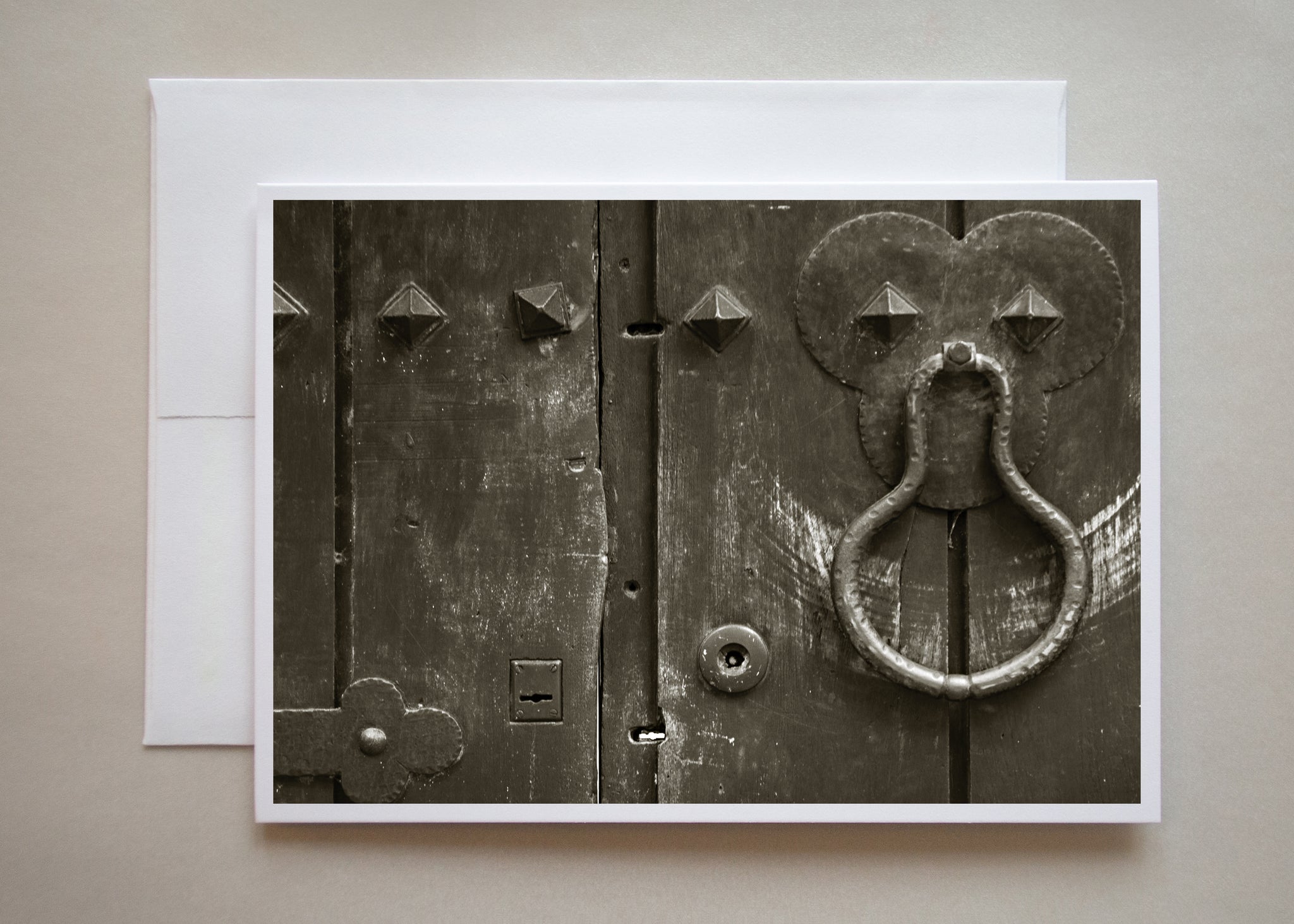 A sepia-toned black and white photograph of a metal door knocker with swing marks against the wooden door photographed in Buenos Aires by Caley Taylor.